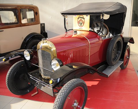 A red tourer with red wheels, a brass radiator and a black hood on a red stand. Opens a larger view
