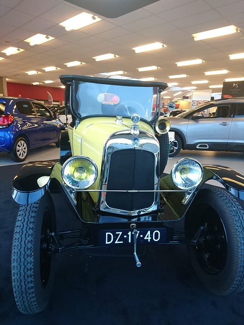 Front view of a narrow car with a flat radiator, two lamps and plate DZ-17-40 under showroom lights. Opens a larger view