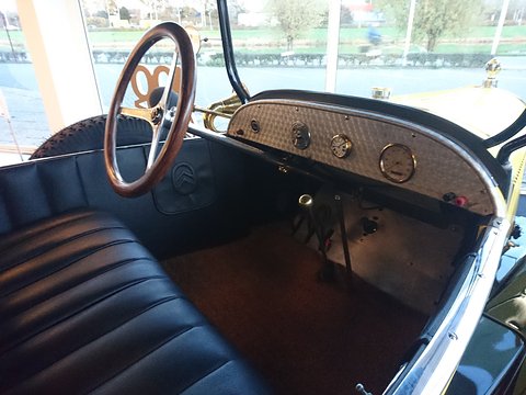 A wooden-rimmed steering wheel, a small instrument panel and a pleated black bench seat inside a yellow car. Opens a larger view