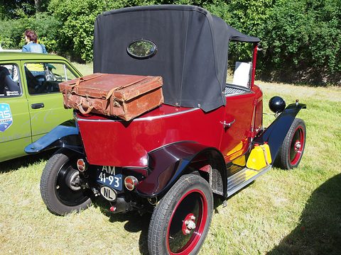 Rear three-quarter view of a red car with a black hood and a brown leather case on its pointed tail. Opens a larger view