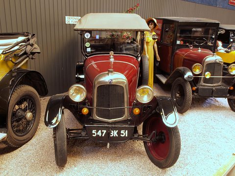 Front view of a red tourer with a nickel radiator, two large lamps and plate 547 GK 51 on a gravel floor. Opens a larger view