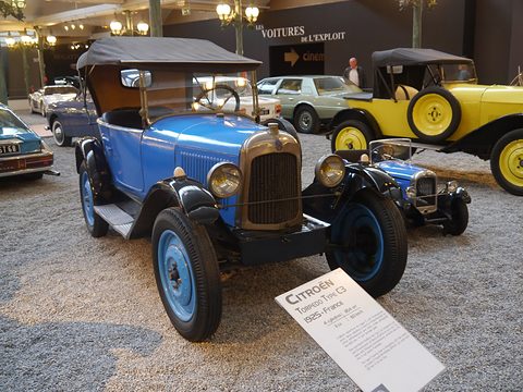 A blue tourer with a black hood and blue wheels on a gravel floor beside its museum label. Opens a larger view