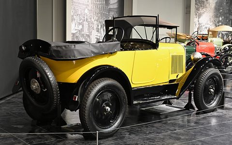Side view of a yellow tourer with black wings and wheels and a folded black hood on a dark tiled floor. Opens a larger view