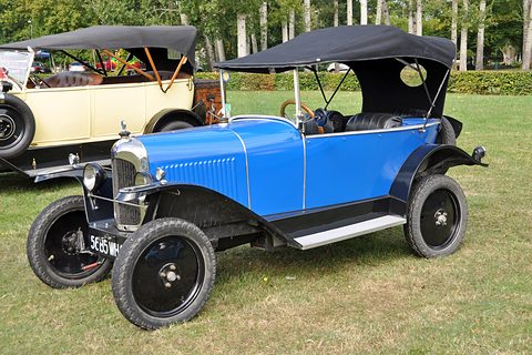 A blue tourer with a black hood and black wings parked on a lawn beside a cream tourer. Opens a larger view