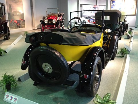 Rear three-quarter view of a yellow car with a black folded hood and a spare wheel on its pointed tail. Opens a larger view