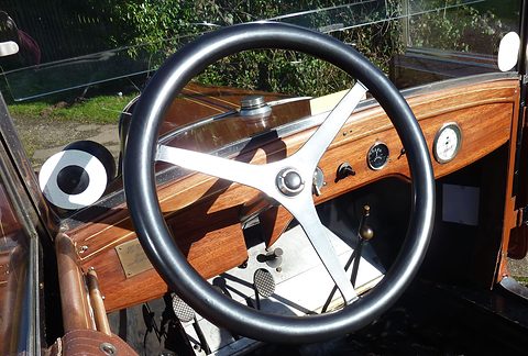 A white-spoked steering wheel in front of a polished mahogany dashboard with two small gauges. Opens a larger view
