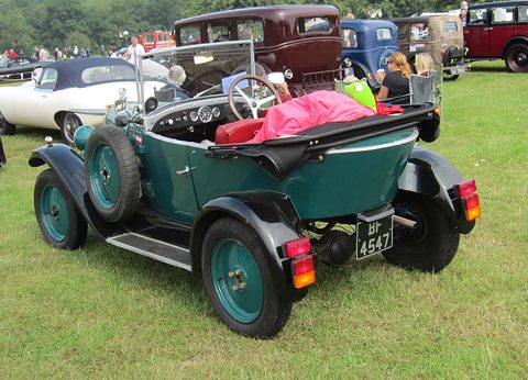Rear three-quarter view of a green open car with a pointed boat-shaped tail and a spare wheel on its flank. Opens a larger view