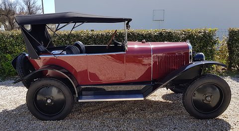 Side view of a maroon open tourer with a black hood and black disc wheels on a gravel drive. Opens a larger view