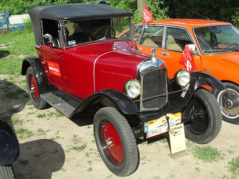 A red tourer with a black hood, red wheels and a rally plate on its bumper, an orange saloon behind. Opens a larger view