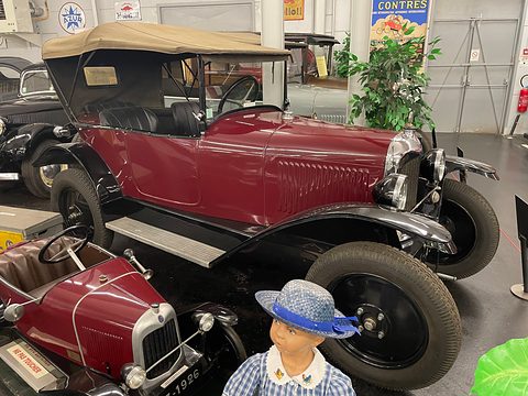 A maroon open three-seater with a beige hood behind a child mannequin and a small pedal car. Opens a larger view