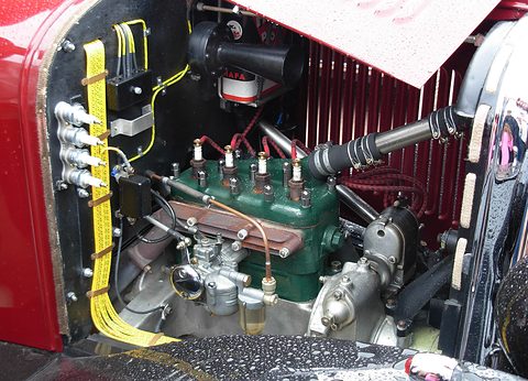 A green four-cylinder engine with yellow wiring, a horn and a carburettor beside a red radiator. Opens a larger view