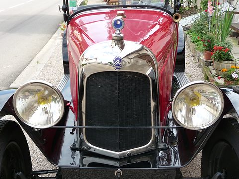 Close front view of a nickel radiator shell with a chevron badge, a motometer and two large headlamps. Opens a larger view