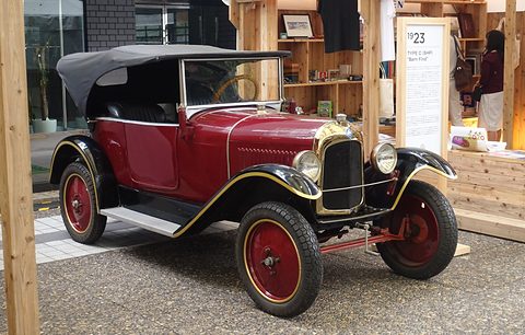 A deep red tourer with gold coachlines, red wheels and a black hood under a wooden canopy. Opens a larger view