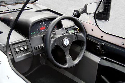 Black three-spoke steering wheel, instrument pod with digital display, toggle switches and a door mirror stalk. Opens a larger view