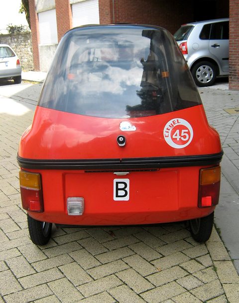 Rear of a narrow red three-wheeler showing two rear wheels, tail lamps, a Belgian B sticker and a 45 disc. Opens a larger view
