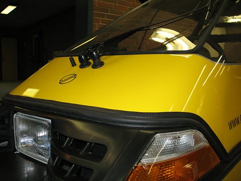 Close view of a yellow bonnet with a black grille, rectangular headlamp, amber indicator and twin wiper spindles. Opens a larger view