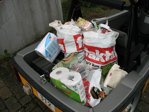Plastic carrier bags, kitchen rolls and groceries filling the open rear tub of a small yellow vehicle. Opens a larger view