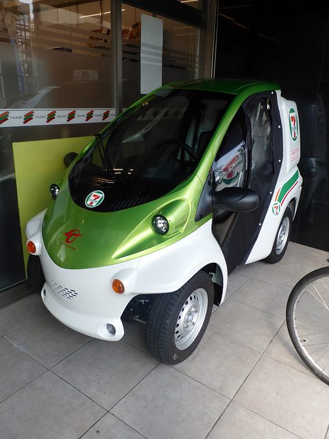 Green and white single-seater with a 7-Eleven door logo parked on tiles under a shop canopy. Opens a larger view