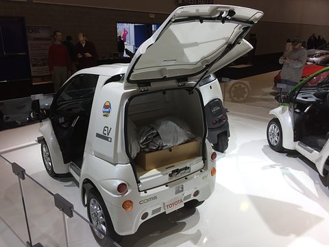 White single-seat microcar with the lid of its large rear cargo box raised, showing a parcel inside. Opens a larger view