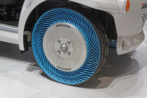 Close view of a blue-spoked airless tyre with a white Bridgestone hub cover under a white car’s wheel arch. Opens a larger view