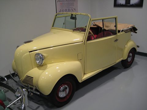 Pale yellow small open car with a V-shaped nose, round headlamps on the wings and a red interior. Opens a larger view