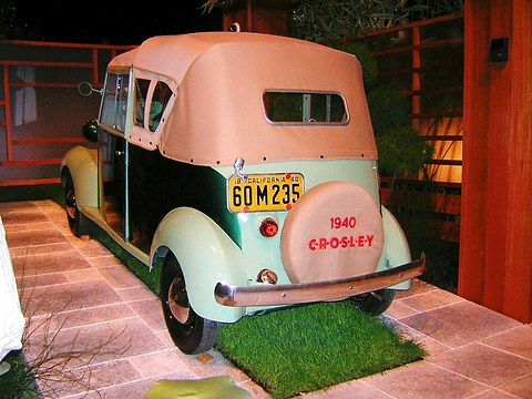 Pale green small car with a peach fabric top and a matching spare-wheel cover lettered 1940 CROSLEY, on a tiled plinth. Opens a larger view