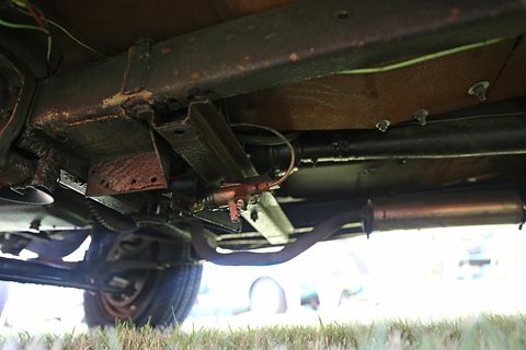 Underside view of a chassis rail, leaf spring and beam axle with brake parts, grass below. Opens a larger view