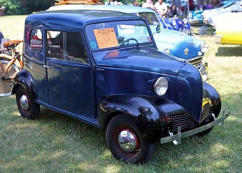 Small dark blue two-door saloon with black wings and a V-shaped nose, parked on grass among other cars. Opens a larger view