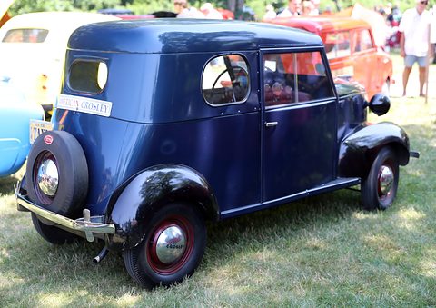 Dark blue small saloon from the right rear, a spare wheel on its tail and a round rear window. Opens a larger view