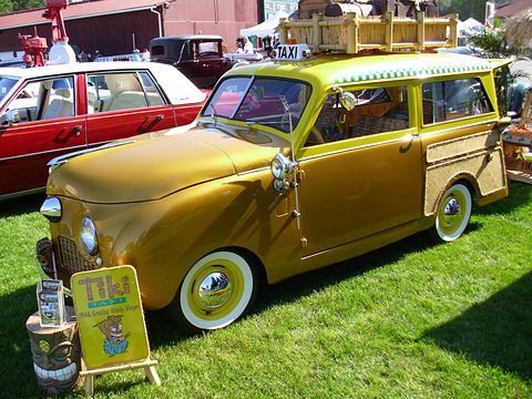 Gold small estate with bamboo trim and a roof rack, a Tiki Taxi sign on the grass in front. Opens a larger view