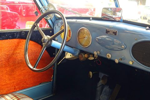 Painted blue metal dashboard with central dials, a large thin-rimmed steering wheel and orange door trim. Opens a larger view