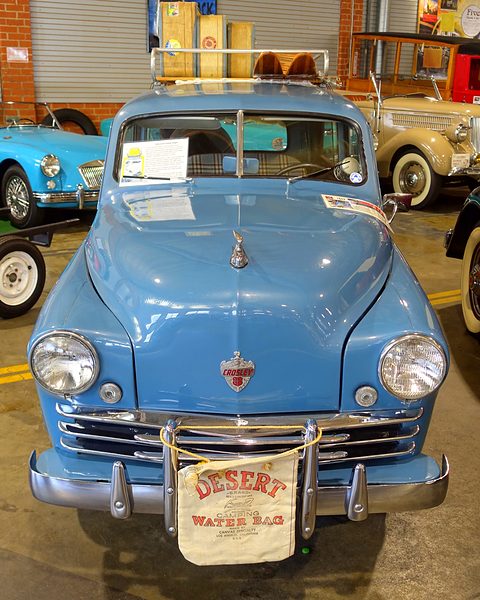 Front of a light blue small estate with a roof rack, a chrome grille and a water bag lettered DESERT. Opens a larger view