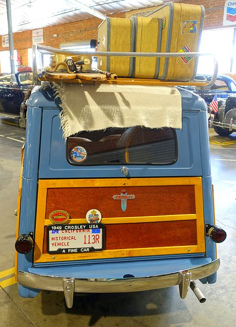 Rear of a light blue estate with a wooden tailgate panel, a 1949 plate and a suitcase on the roof rack. Opens a larger view