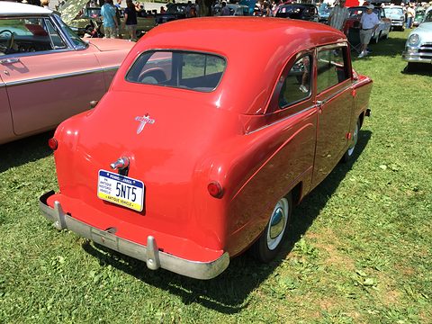 Red small saloon from the left rear with a chrome bumper and a Pennsylvania plate, on a show field. Opens a larger view