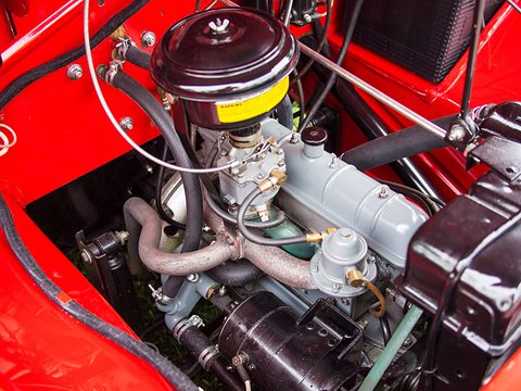 Engine bay with a small four-cylinder engine, round air cleaner, carburettor and red bodywork around it. Opens a larger view