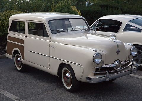 Cream small estate with brown woodgrain panels and a propeller-centred grille, a white car beside it. Opens a larger view