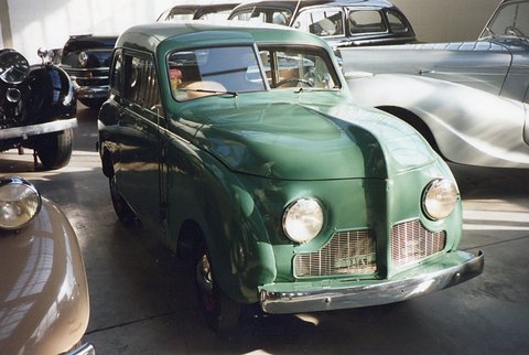 Green slab-sided small saloon with a chrome grille, seen from the front among old cars in a museum. Opens a larger view