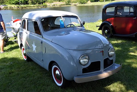 Silver slab-sided small saloon with a white star on its door, round headlamps and a simple grille, a lake behind.