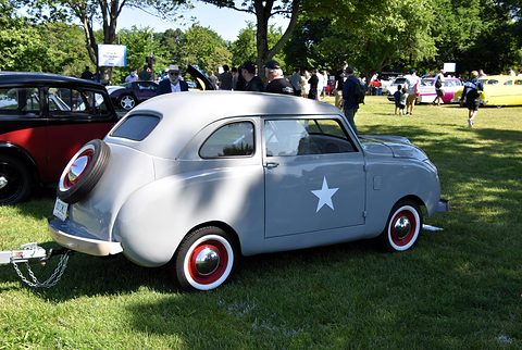 Silver small saloon from the left rear with a spare-wheel cover and a white star on the door, on a lawn. Opens a larger view