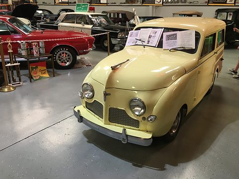 Cream small estate with woodgrain side panels and round headlamps, other cars and display boards around it. Opens a larger view