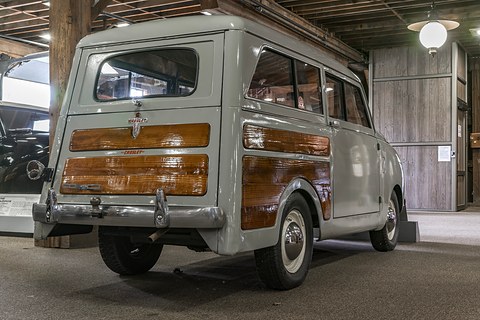 Grey small estate from the left rear, woodgrain on the tailgate and sides, in a timber-framed hall. Opens a larger view