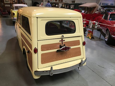 Rear of a cream small estate with a split tailgate carrying woodgrain panels, red cars beside it. Opens a larger view