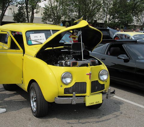 Bright yellow small estate with its bonnet open and twin headlamps, parked on tarmac among other cars. Opens a larger view