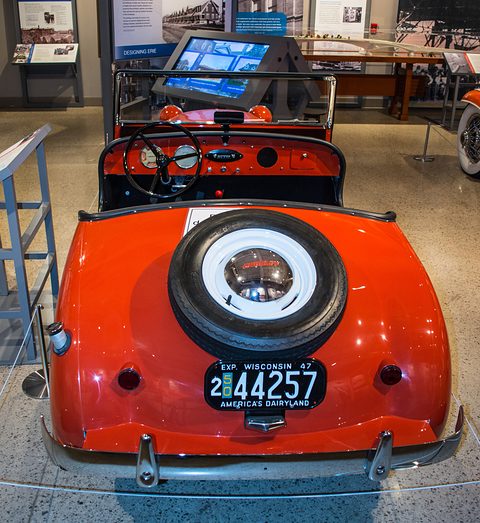 Rear of an orange roadster with a spare wheel on its tail and a 1947 Wisconsin plate. Opens a larger view