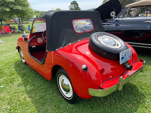 Red roadster from the left rear with the black top up and a spare wheel on the sloping tail. Opens a larger view