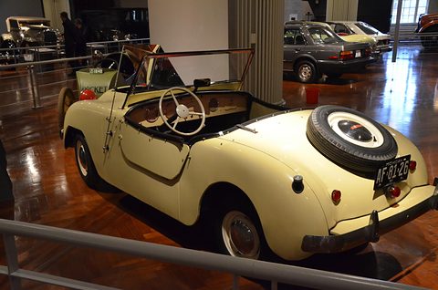 Cream roadster from the left rear with its spare wheel on the tail and a pale steering wheel. Opens a larger view