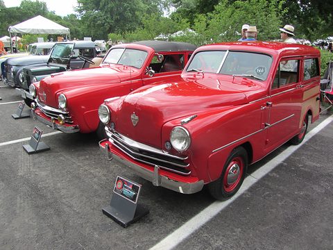 Two red small cars, a saloon and an estate, parked side by side on tarmac with display signs. Opens a larger view