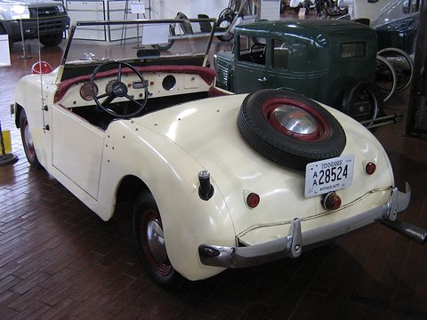 White roadster from the rear with a spare wheel on the tail, a Tennessee plate and a door on its flank. Opens a larger view