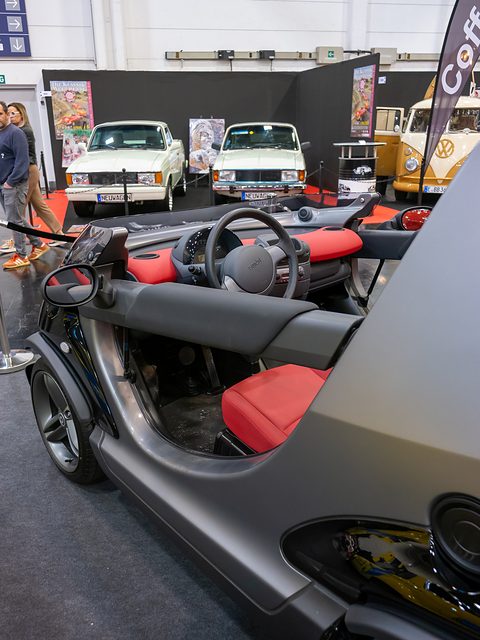 Close view along the side of a grey doorless car, showing the bar across the opening, a red seat and the steering wheel.
