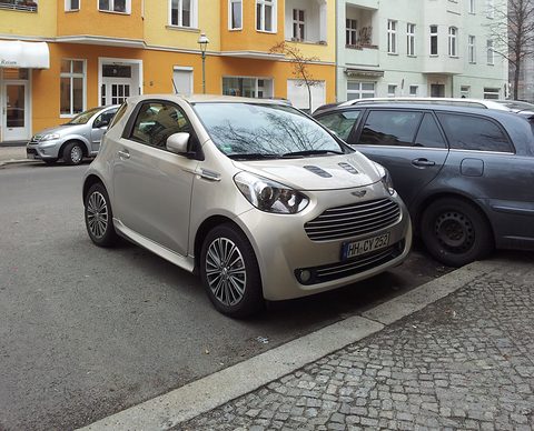 Silver city car parked at an angle on cobbles in front of an orange apartment block. Opens a larger view